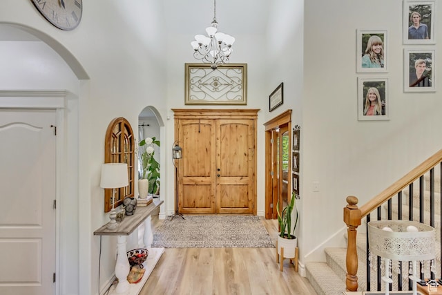 foyer entrance featuring arched walkways, a high ceiling, wood finished floors, a chandelier, and stairway