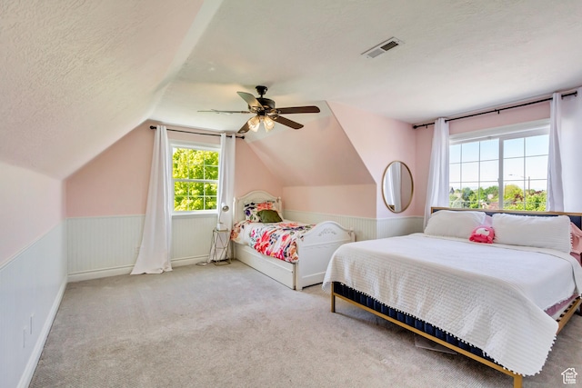 carpeted bedroom featuring a wainscoted wall, lofted ceiling, a ceiling fan, and a textured ceiling