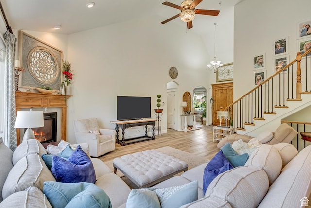 living area with high vaulted ceiling, arched walkways, a glass covered fireplace, ceiling fan, and wood finished floors
