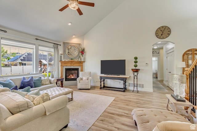 living area with high vaulted ceiling, ceiling fan, arched walkways, wood finished floors, and a glass covered fireplace