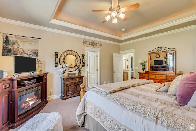 bedroom featuring a tray ceiling, light colored carpet, ornamental molding, a ceiling fan, and a glass covered fireplace