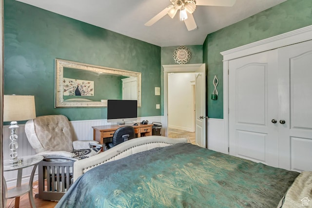 bedroom with a wainscoted wall, a closet, and a ceiling fan