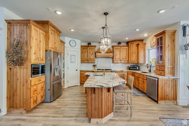 kitchen featuring appliances with stainless steel finishes, a sink, an island with sink, light wood-style floors, and a kitchen bar