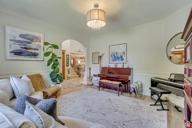 living area featuring crown molding, arched walkways, wood finished floors, stairs, and wainscoting