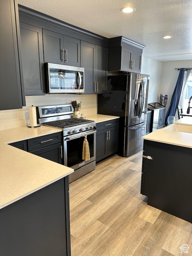 kitchen featuring stainless steel appliances, a sink, a textured ceiling, light wood-type flooring, and recessed lighting