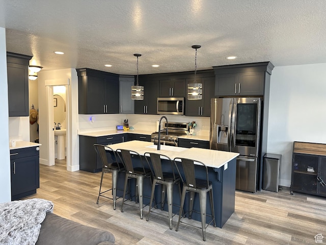 kitchen featuring stainless steel appliances, light wood-style floors, a breakfast bar, a textured ceiling, and light countertops