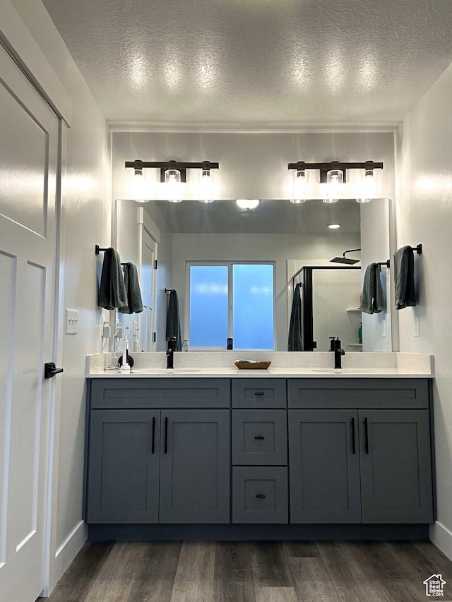 full bathroom with a textured ceiling, wood finished floors, a stall shower, double vanity, and baseboards