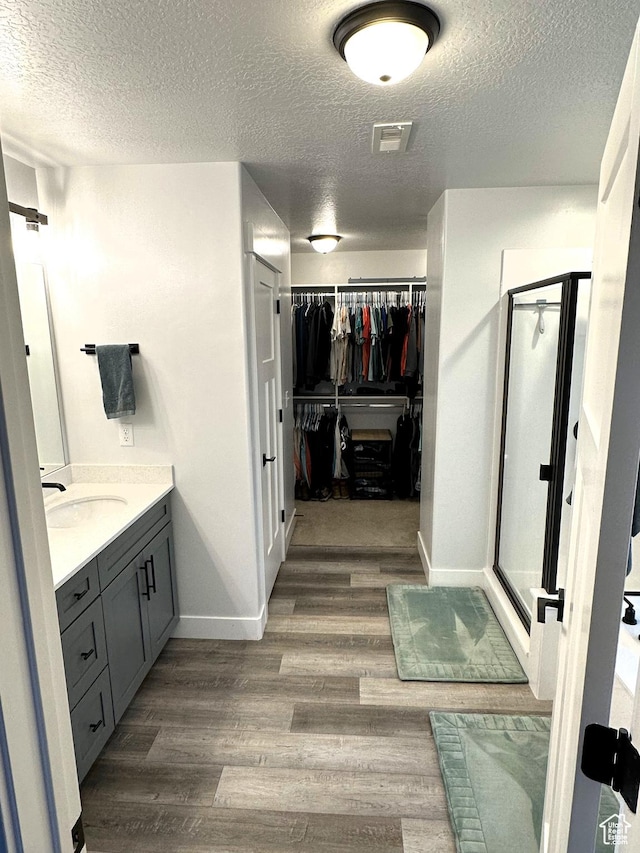bathroom with a textured ceiling, wood finished floors, a stall shower, a spacious closet, and vanity