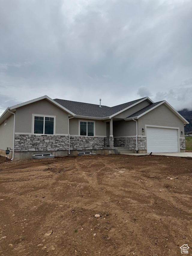 single story home with stone siding, an attached garage, and stucco siding