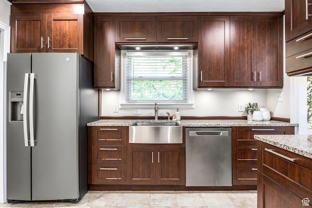 kitchen with appliances with stainless steel finishes, a sink, light stone counters, and dark brown cabinetry