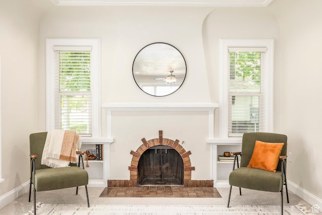 sitting room with a brick fireplace, baseboards, ceiling fan, and ornamental molding