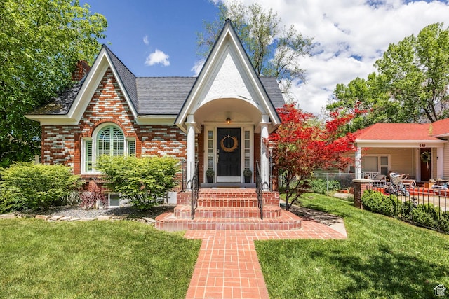 tudor home with a front yard, brick siding, and roof with shingles