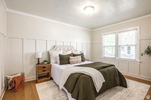 bedroom with a decorative wall, a textured ceiling, wood finished floors, and a wainscoted wall