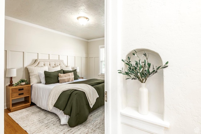bedroom featuring a textured ceiling, wood finished floors, crown molding, wainscoting, and a decorative wall