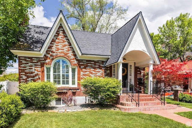 tudor house featuring a front yard, brick siding, and a shingled roof