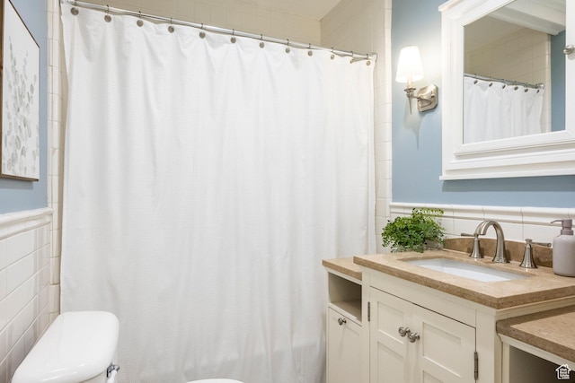 bathroom with tile walls, toilet, wainscoting, vanity, and a shower with curtain