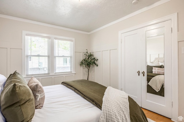 bedroom with a decorative wall, light wood finished floors, crown molding, a wainscoted wall, and a textured ceiling