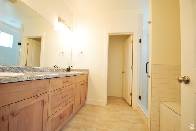 full bathroom with a shower stall, double vanity, tiled tub, and baseboards