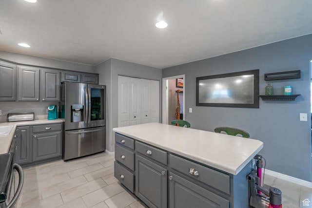 kitchen with stainless steel refrigerator with ice dispenser, gray cabinetry, light tile patterned flooring, baseboards, and recessed lighting