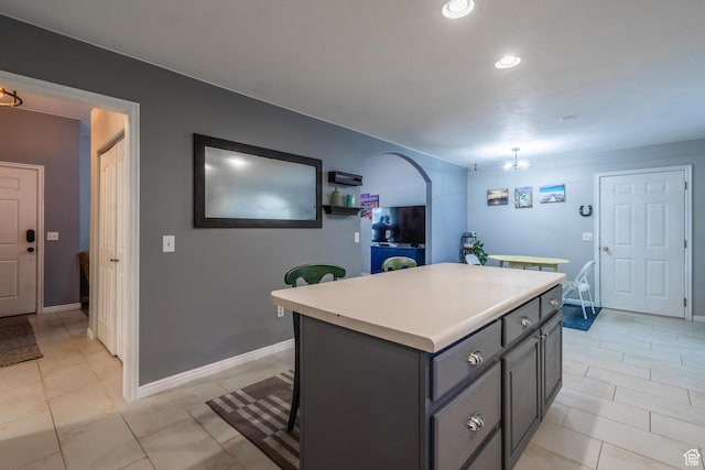 kitchen featuring a kitchen island, light countertops, arched walkways, light tile patterned floors, and baseboards