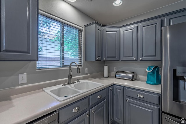 kitchen featuring stainless steel refrigerator with ice dispenser, a sink, gray cabinetry, light countertops, and dishwashing machine