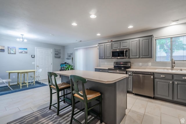 kitchen featuring appliances with stainless steel finishes, gray cabinetry, a sink, a breakfast bar, and a kitchen island