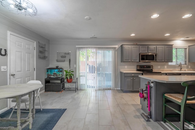 kitchen with gray cabinetry, stainless steel appliances, light countertops, a sink, and recessed lighting