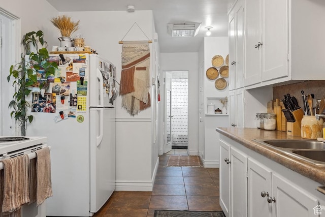 kitchen with white appliances, white cabinets, a sink, dark tile patterned floors, and baseboards