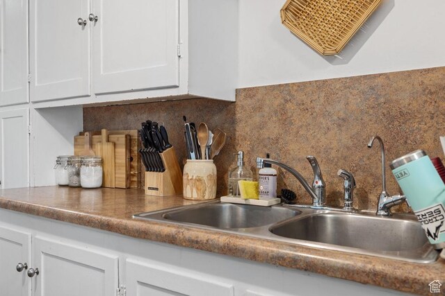 kitchen view of white cabinets, a sink, decorative backsplash, and dark countertops