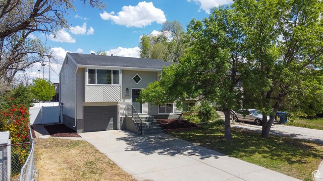 split foyer home featuring concrete driveway, fence, an attached garage, and a gate