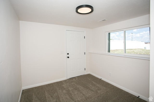 empty room featuring dark colored carpet and baseboards
