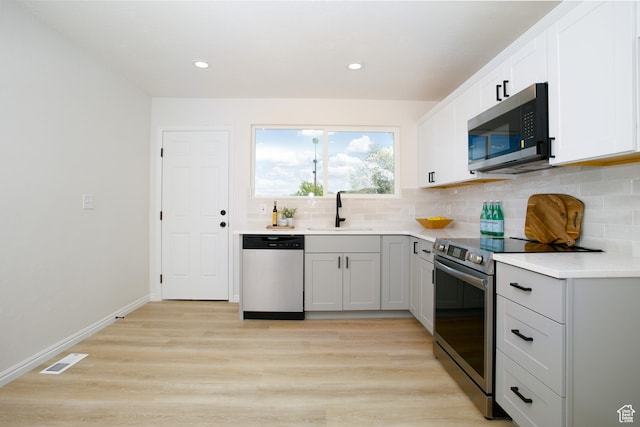 kitchen with stainless steel appliances, a sink, decorative backsplash, light wood-style floors, and recessed lighting