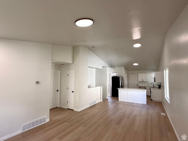 kitchen featuring freestanding refrigerator, vaulted ceiling, light wood-style flooring, a kitchen island, and white cabinets