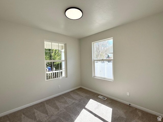 spare room with healthy amount of natural light, dark carpet, and baseboards