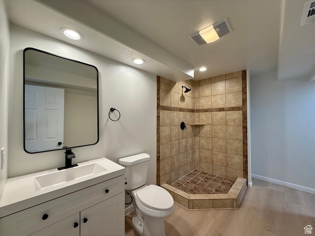 bathroom with toilet, wood finished floors, tiled shower, vanity, and recessed lighting