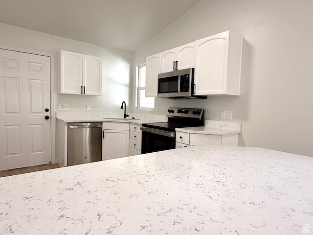 kitchen with stainless steel appliances, a sink, vaulted ceiling, white cabinets, and light stone countertops
