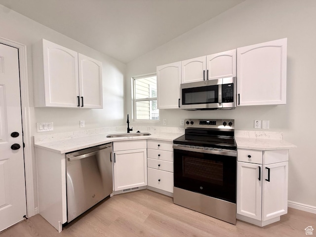 kitchen featuring appliances with stainless steel finishes, a sink, light wood-style floors, vaulted ceiling, and white cabinetry