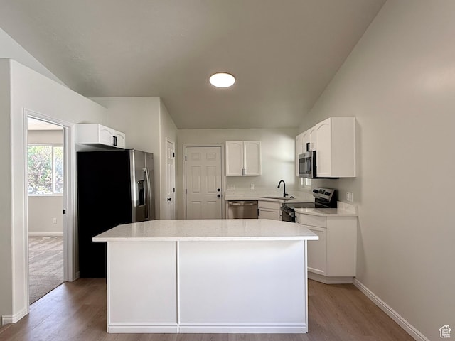 kitchen with stainless steel appliances, a sink, light wood finished floors, baseboards, and lofted ceiling