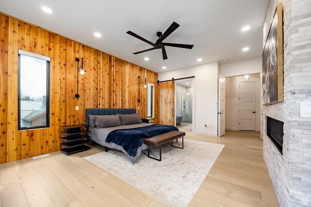 9335 N Canopy Ln E, Sundance, UT 84604 - bedroom featuring a barn door, wooden walls, light wood-style floors, ensuite bath, and a stone fireplace