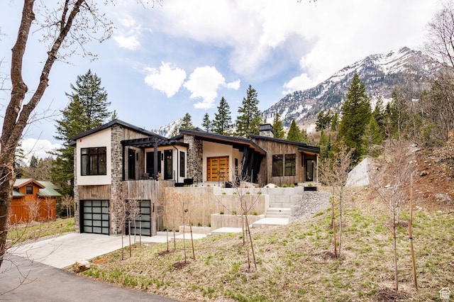 9335 N Canopy Ln E, Sundance, UT 84604 - modern home featuring stone siding, concrete driveway, a mountain view, a chimney, and a garage
