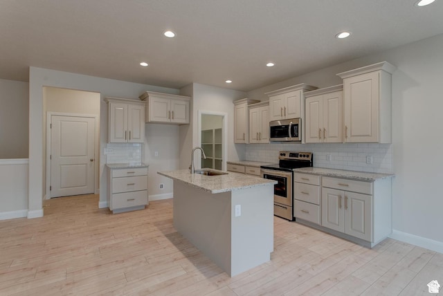 2318 E 320 N Unit 01, Spanish Fork, UT 84660 - kitchen featuring stainless steel appliances, backsplash, light wood-style flooring, light stone countertops, and a kitchen island with sink