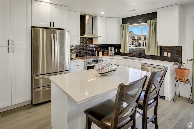 kitchen with appliances with stainless steel finishes, wall chimney exhaust hood, a sink, light wood-style floors, and recessed lighting