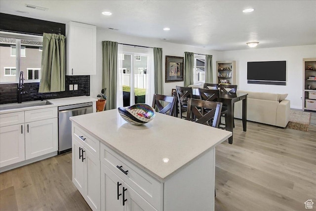 kitchen featuring stainless steel dishwasher, a sink, light wood-style flooring, a center island, and decorative backsplash