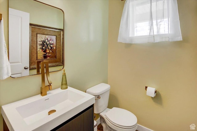half bathroom featuring toilet, vanity, and baseboards