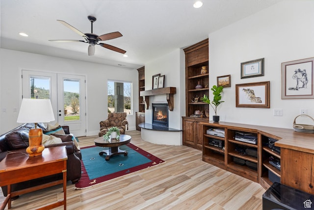 living area featuring a lit fireplace, ceiling fan, recessed lighting, french doors, and light wood-style flooring
