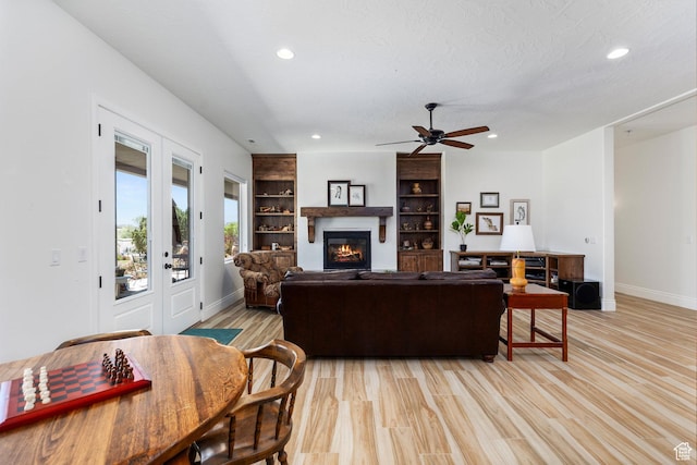 living area featuring a glass covered fireplace, baseboards, recessed lighting, ceiling fan, and light wood-style flooring