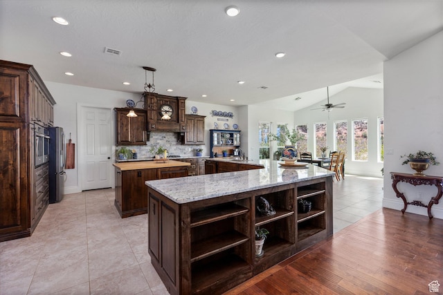 kitchen featuring open shelves, a spacious island, stainless steel appliances, dark brown cabinets, and backsplash