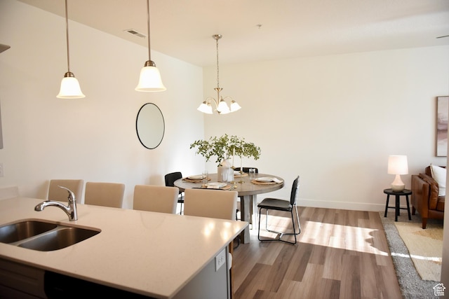 kitchen featuring a sink, wood finished floors, hanging light fixtures, baseboards, and a chandelier