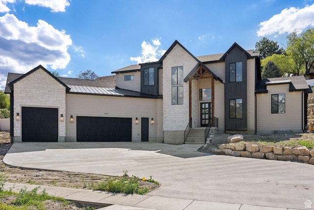 modern home with a garage, a standing seam roof, concrete driveway, stone siding, and metal roof