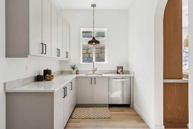 bar area with dishwasher, a sink, arched walkways, light wood-style flooring, and decorative light fixtures